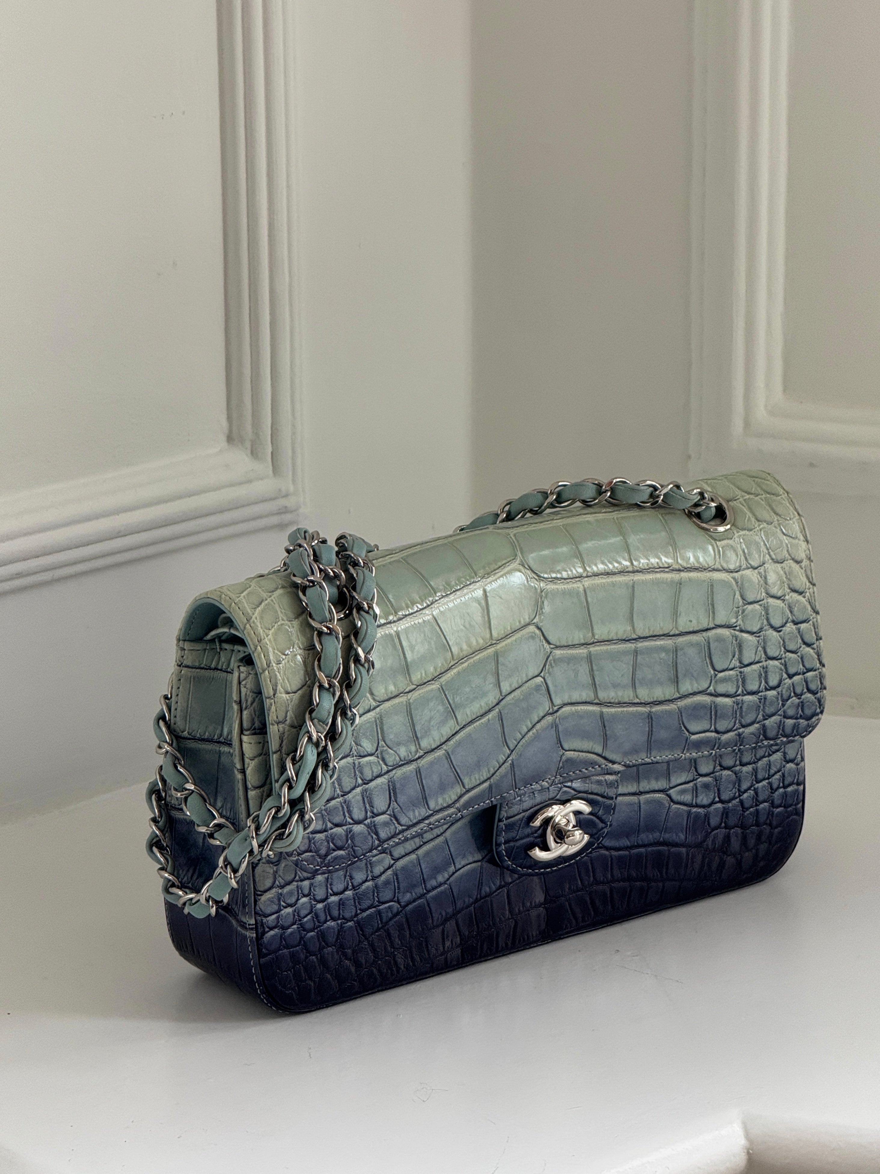 Blue and green crocodile-patterned handbag with a chain detail on a white surface.